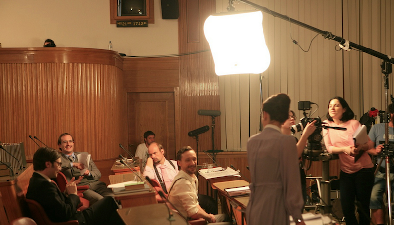 Production still from “The Fruits of our Land” shot inside the National Assembly of the Republic of Slovenia. Artist/Director Jasmina Cibic is on the far right. Photo by Pete Moss courtesy of the artist and Galerija Škuc, © Jasmina Cibic, All Rights Reserved.